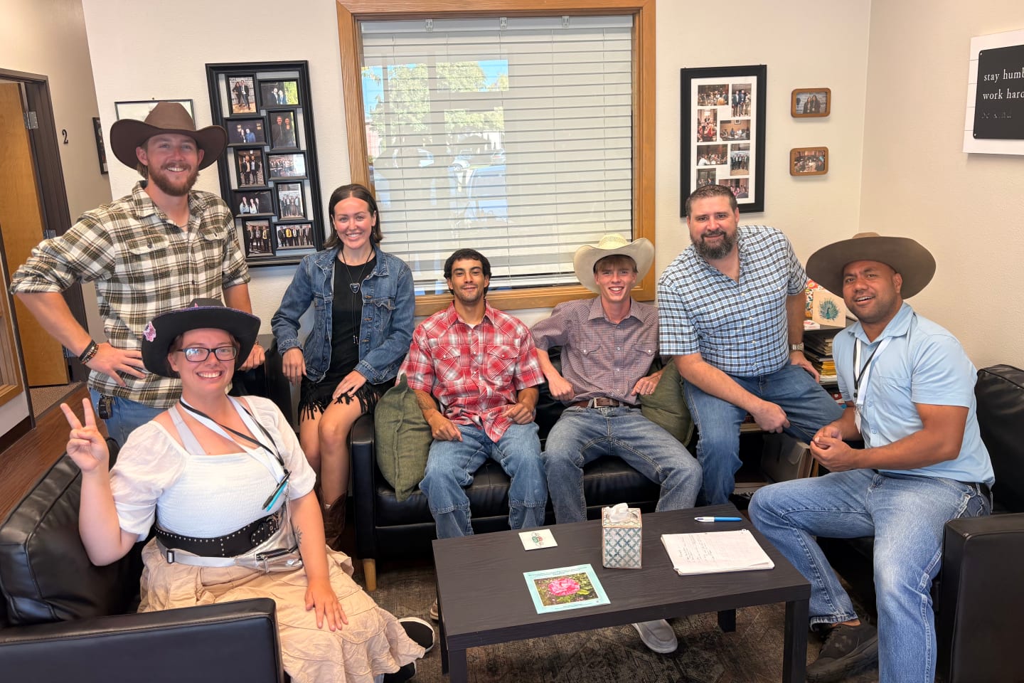 Seven Iron Bloom team members on the office couches for western day, several in cowboy hats and plaid shirts, smiling at the camera